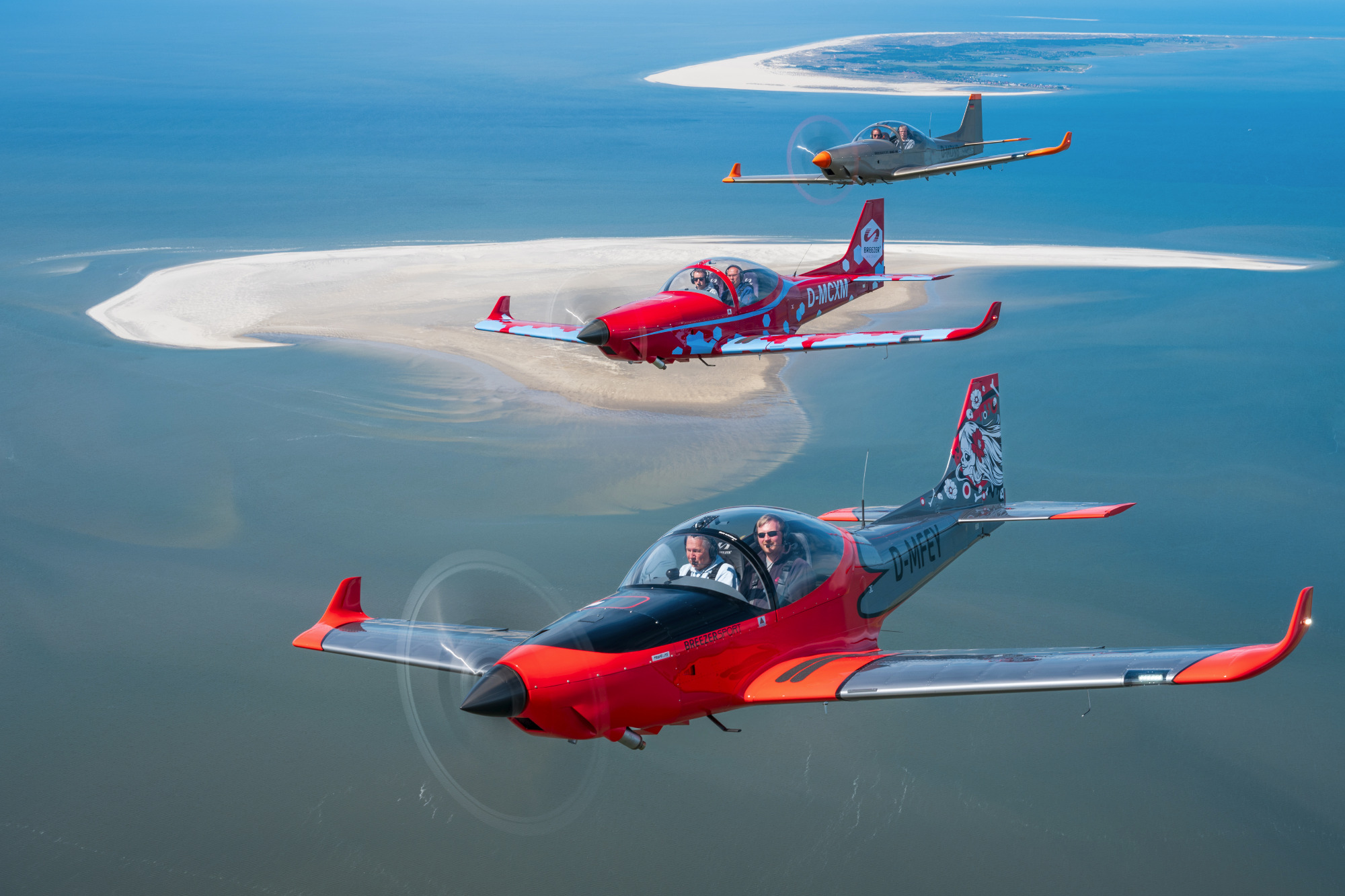 Drei Trainingsflugzeuge fliegen über einer Sandbank im Wasser.