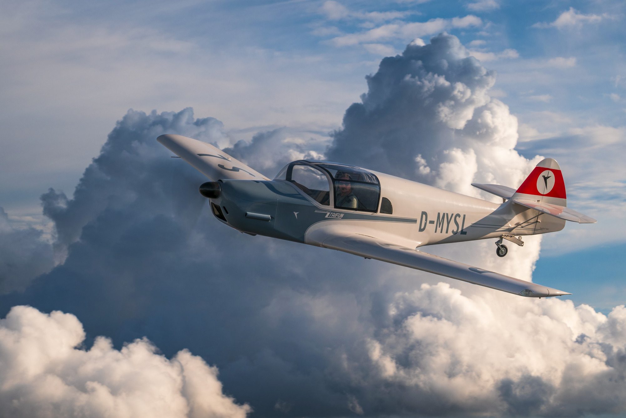 Ein kleines Flugzeug fliegt über große, weiße Wolken.