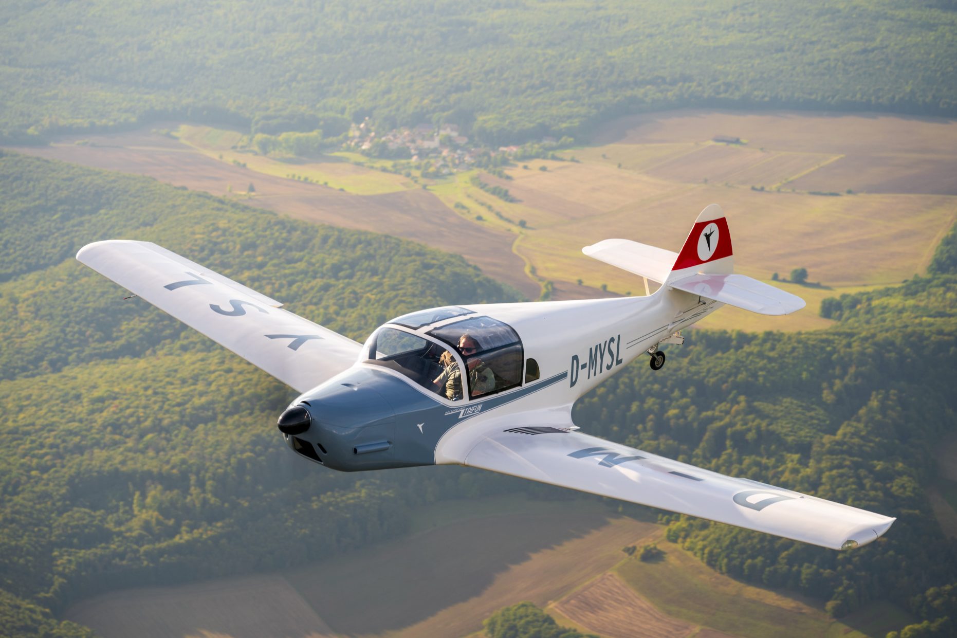 Ein Kleinflugzeug fliegt über grüne Felder und Wälder.