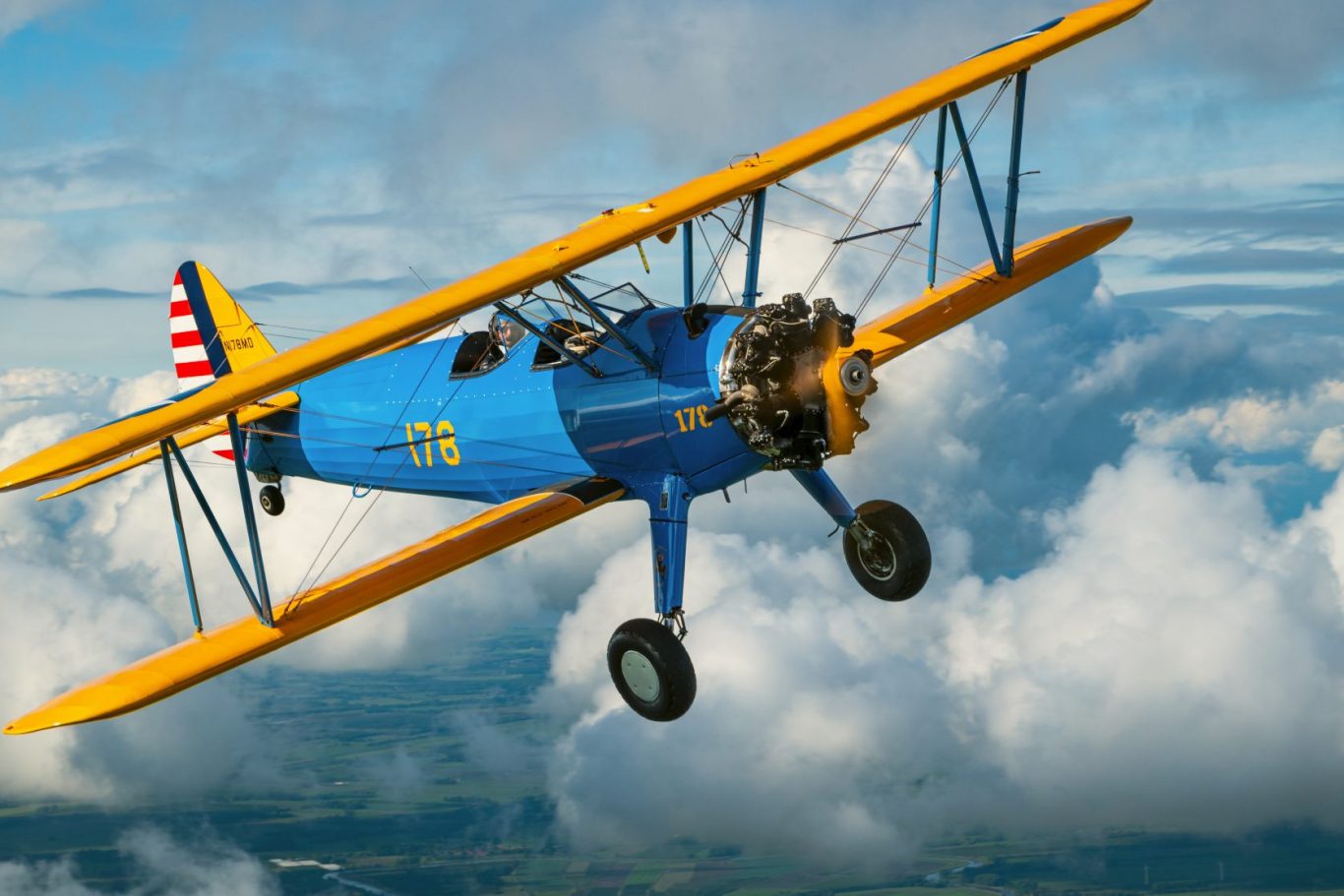 Luftbild einer Boeing Stearman über wolkenreicher Landschaft Ein blauer Doppeldecker mit gelben Flügeln fliegt über wolkenreiche Landschaft.