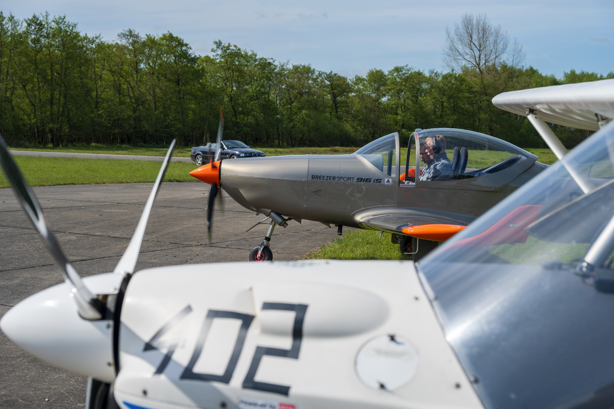 Zwei Flugzeuge auf einem Flugplatz, eines mit orangefarbenem Propeller.